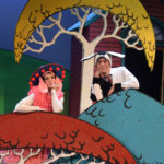 Miriam Gutierrez and Al Kroeten in Go Dog Go, dressed in dog costumes and perched in cartoon-like trees