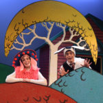 Miriam Gutierrez and Al Kroeten in Go Dog Go, dressed in dog costumes and perched in cartoon-like trees