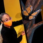 Tamia Renée as the Monarch butterfly in HOW TO BUILD AN ARK. PHOTO DESCRIPTION: A female actor wearing a black costume and orange face mask holds up an orange and black Monarch butterfly puppet.